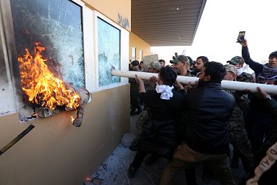 Members of an Iraqi Shiite militia and their supporters attack the entrance of the U.S. Embassy compound in Baghdad on Tuesday, Dec. 31, 2019.