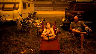 Image: Amy and Ben Spencer sit at a Bega campground after being evacuated f