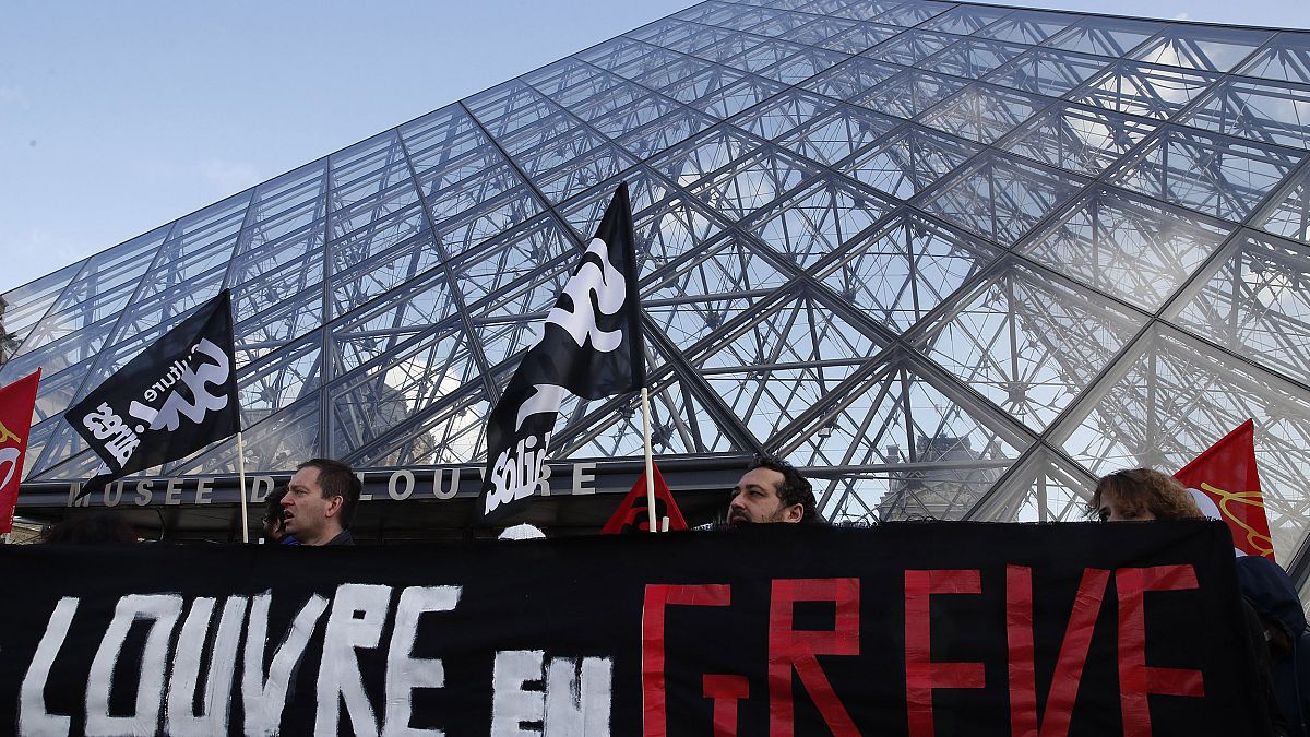 Image: Striking employees hold a banner reading "Louvre on strike" outside 