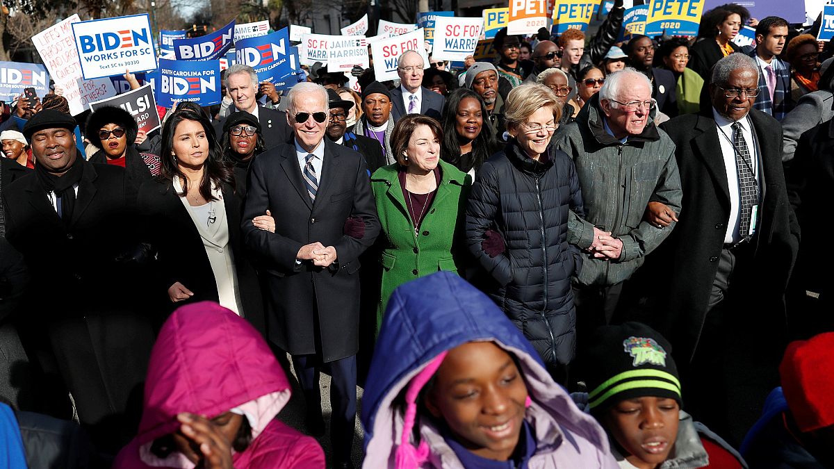 Image: Seven of the democratic U.S. 2020 presidential candidates walk arm-i
