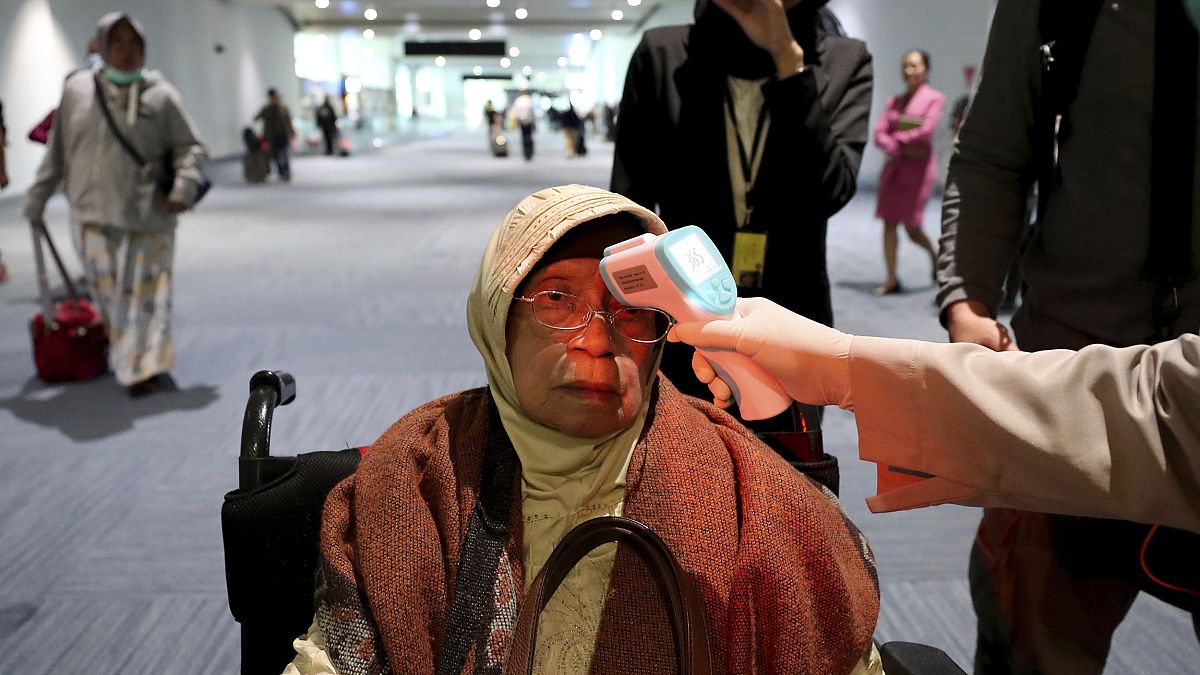 Image: A health official scans the body temperature of a passenger as she a