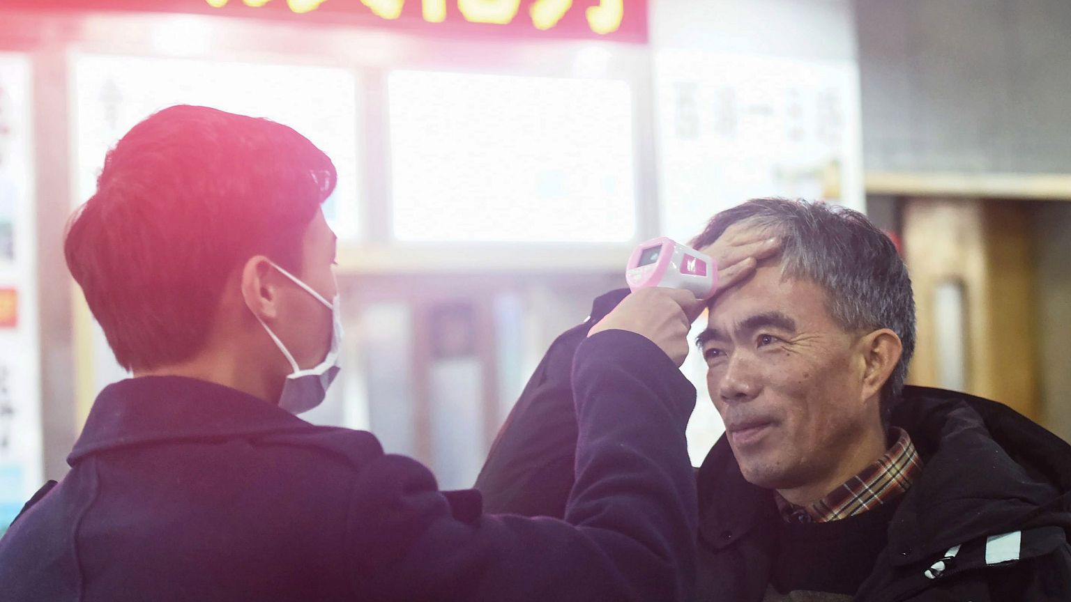 Image: A staff member checks the body temperature of a passenger after a tr
