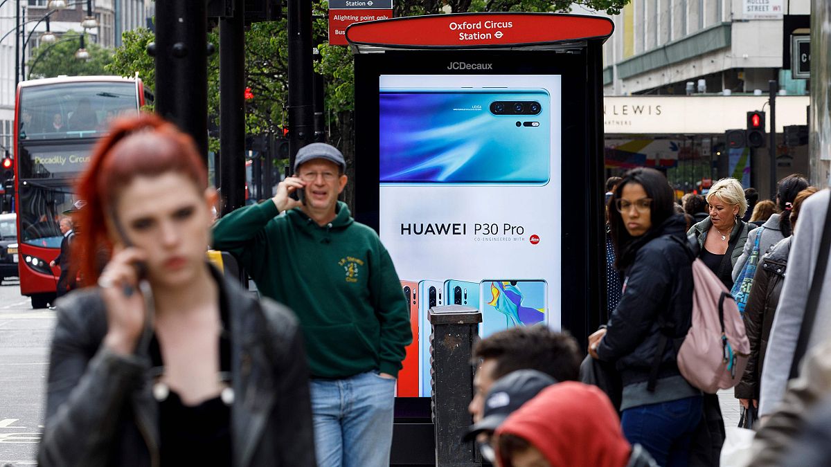 Image: Pedestrians use their mobile phones near a Huawei advert at a bus st