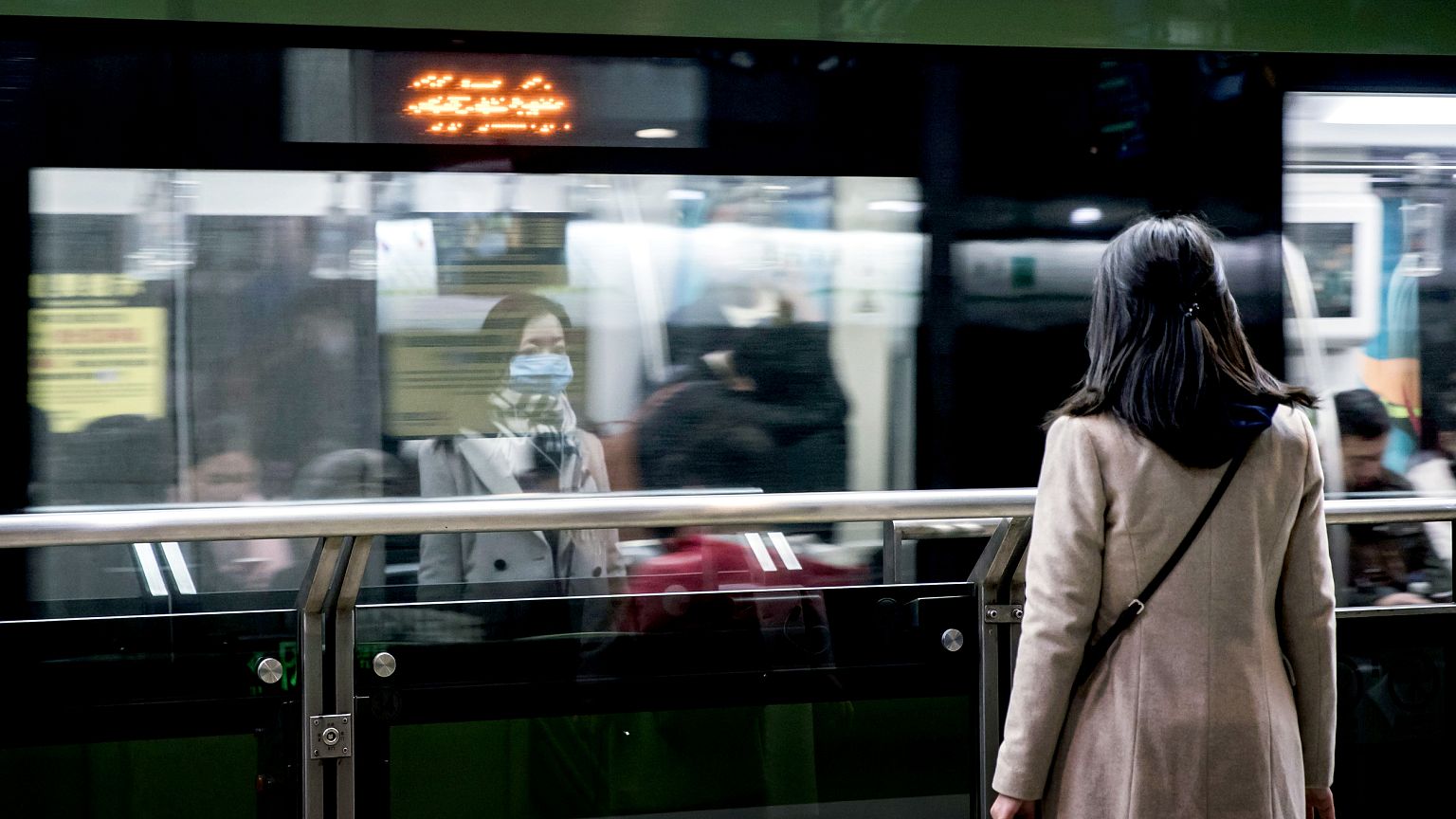 Image: A woman wears a protective mask while waiting for the subway in the 