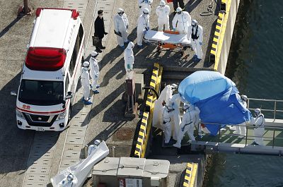 Officers in protective gear escort a person (under the blue sheet) to a maritime police base in Yokohama, south of Tokyo on Feb. 4, 2020. The person was on board cruise ship Diamond Princess and was tested positive for coronavirus.