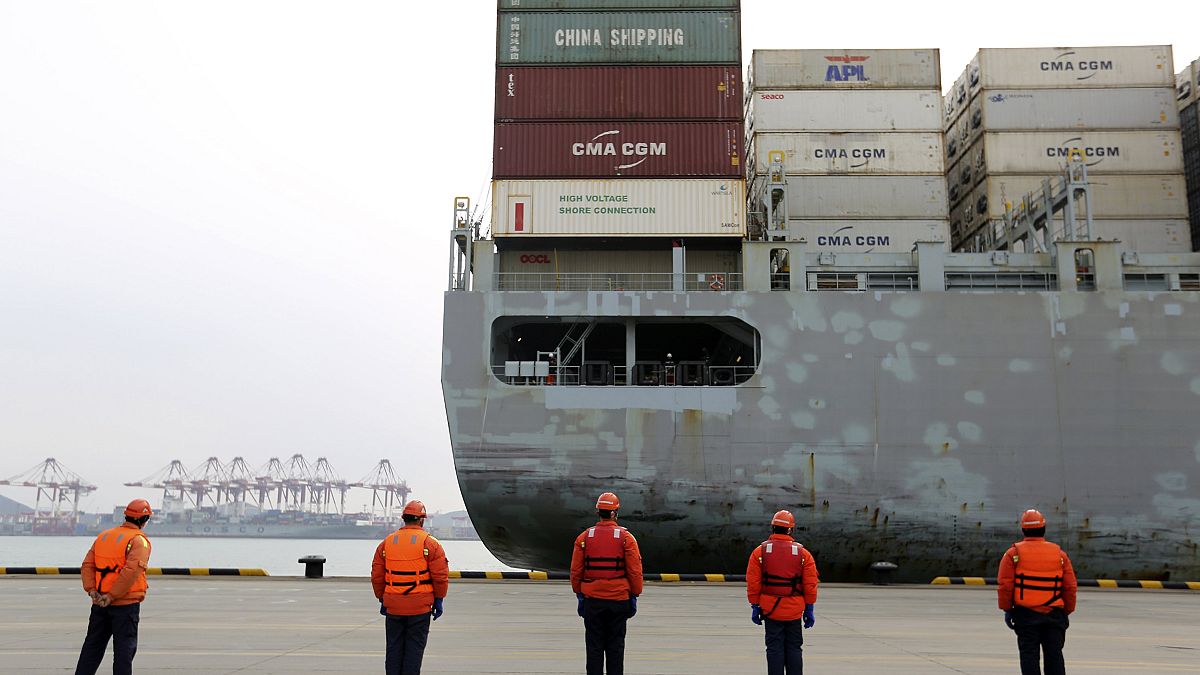 Image: Workers watch a container ship arrive at a port in Qingdao in east C