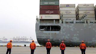 Image: Workers watch a container ship arrive at a port in Qingdao in east C