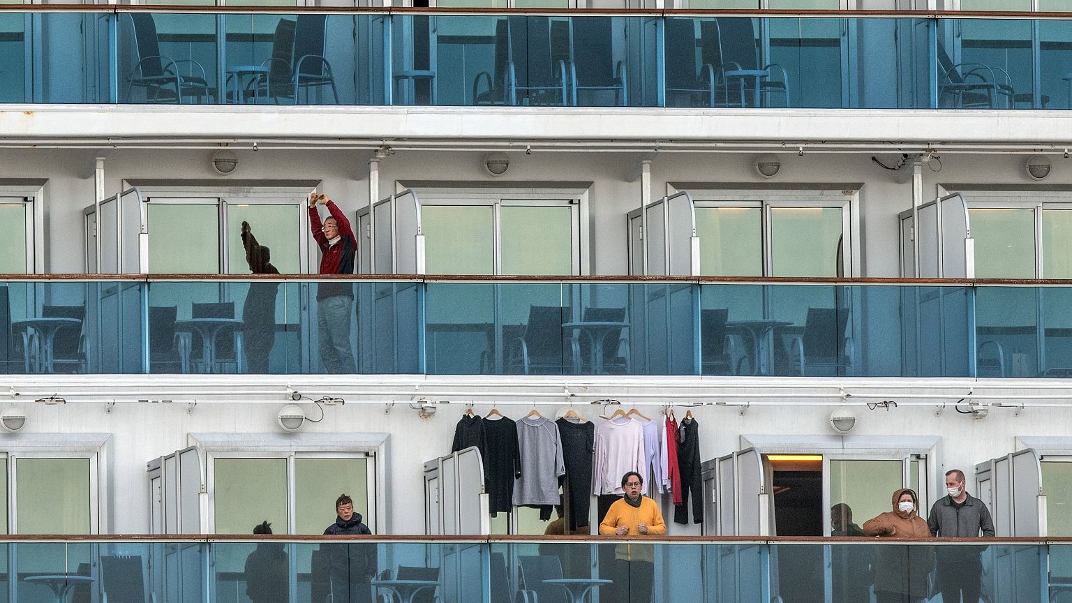 Image: A passenger jogs on the spot as another stretches as they wait on th