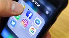Image: A man holds a smart phone with the icons for the social networking a