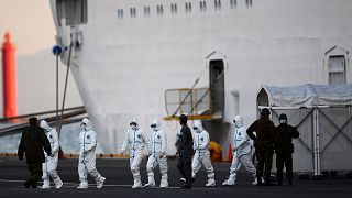 Image: People wearing protective suits walk from the Diamond Princess cruis