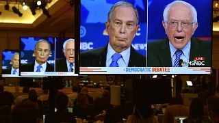 Image: Mike Bloomberg and Senator Bernie Sanders on video screens in the me
