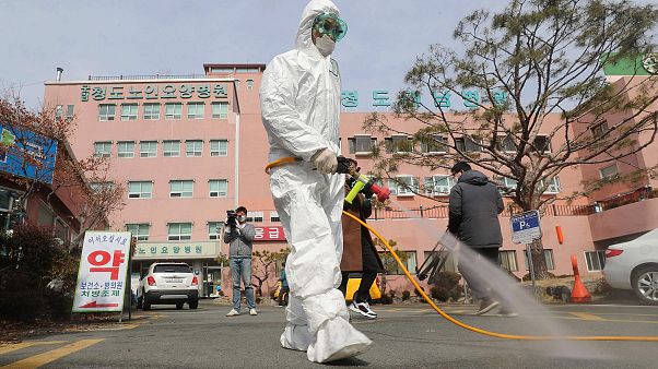 Image: A South Korean health official sprays disinfectant in front of a hos Image: A South Korean health official sprays disinfectant in front of a hos