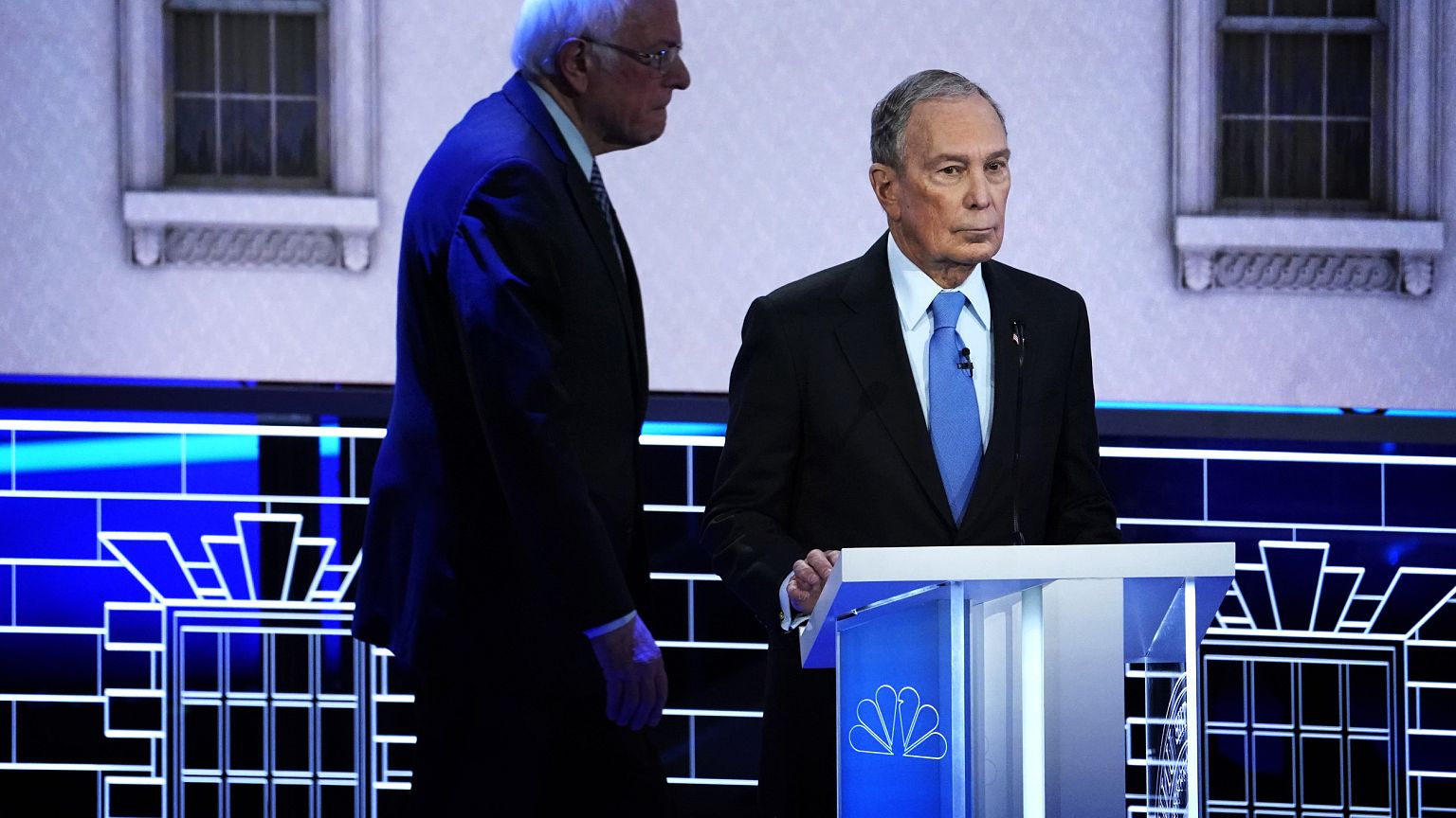 Image: Sen. Bernie Sanders walks behind Mike Bloomberg at a Democratic pres
