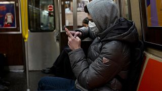 Image: A man wearing a face mask reads his phone on the subway in New York 