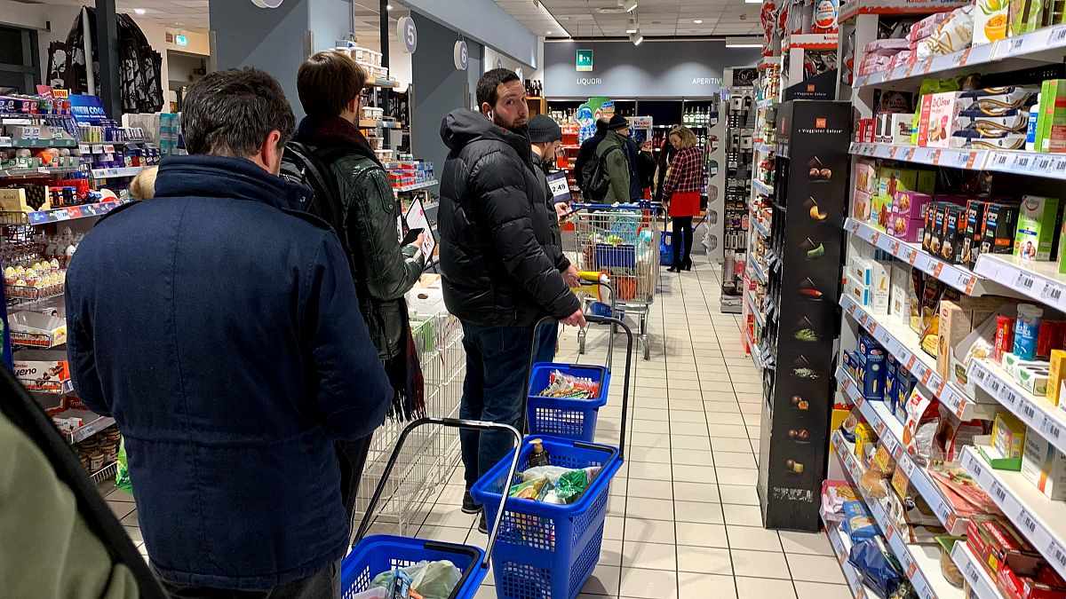 Image: Customers wait in line to pay at a supermarket in Milan on March 7, 