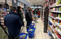 Image: Customers wait in line to pay at a supermarket in Milan on March 7,