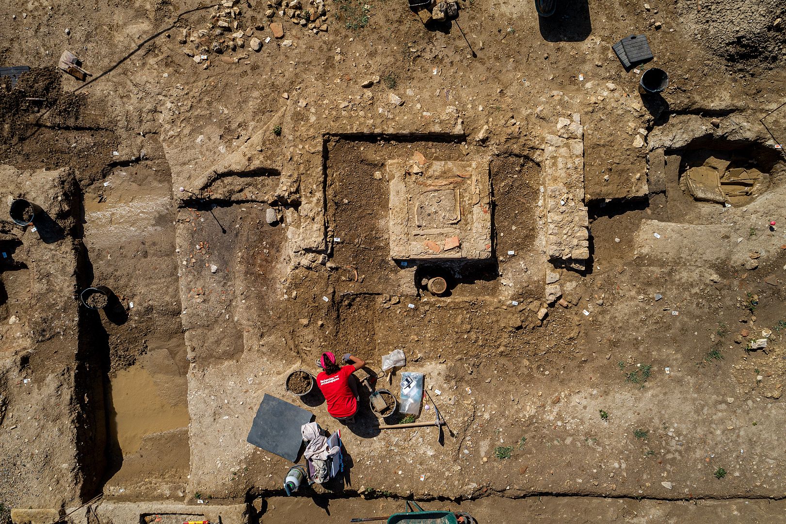 Petit monument conservé en élévation et tombe à crémation au sein d’un enclos maçonné quadrangulaire. Le monument englobe une tombe en coffrage de tuiles