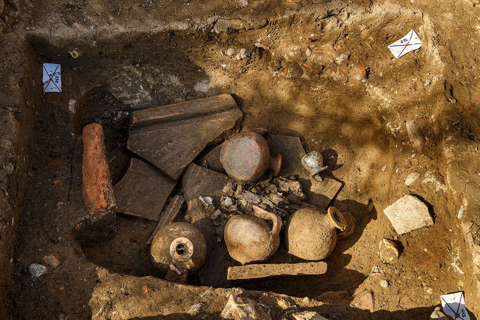 Tombe à crémation constituée d’un amas d’ossements humains brûlés surmonté de cruches en céramique et d’un petit balsamaire en verre.