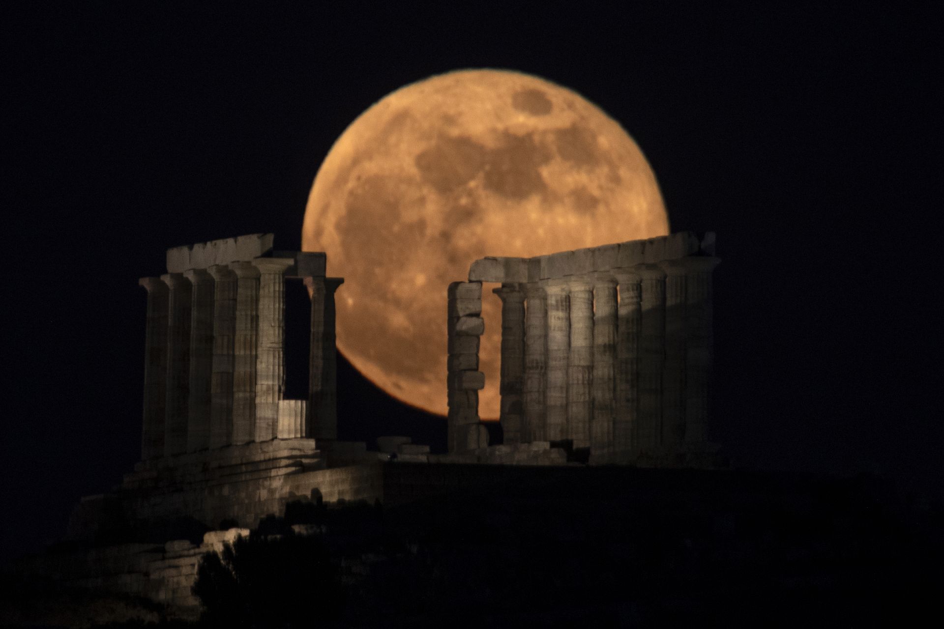The flower supermoon rises behind the columns of the ancient marble temple of Poseidon at Cape Sounion, about 70 Km south of Athens. May 26, 2021 