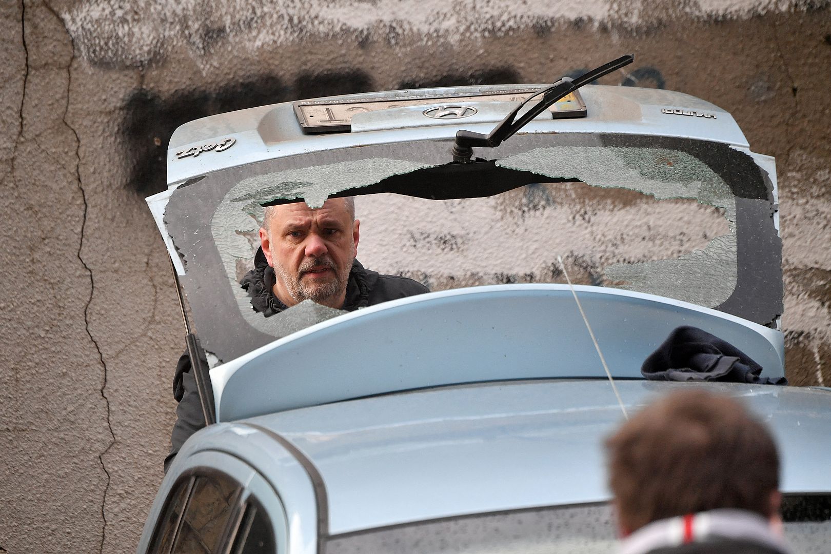 A local resident inspects his damaged car at the site of fallen fragments of Russian rocket, near a multi-storey residential building in Kyiv. March 9, 2023