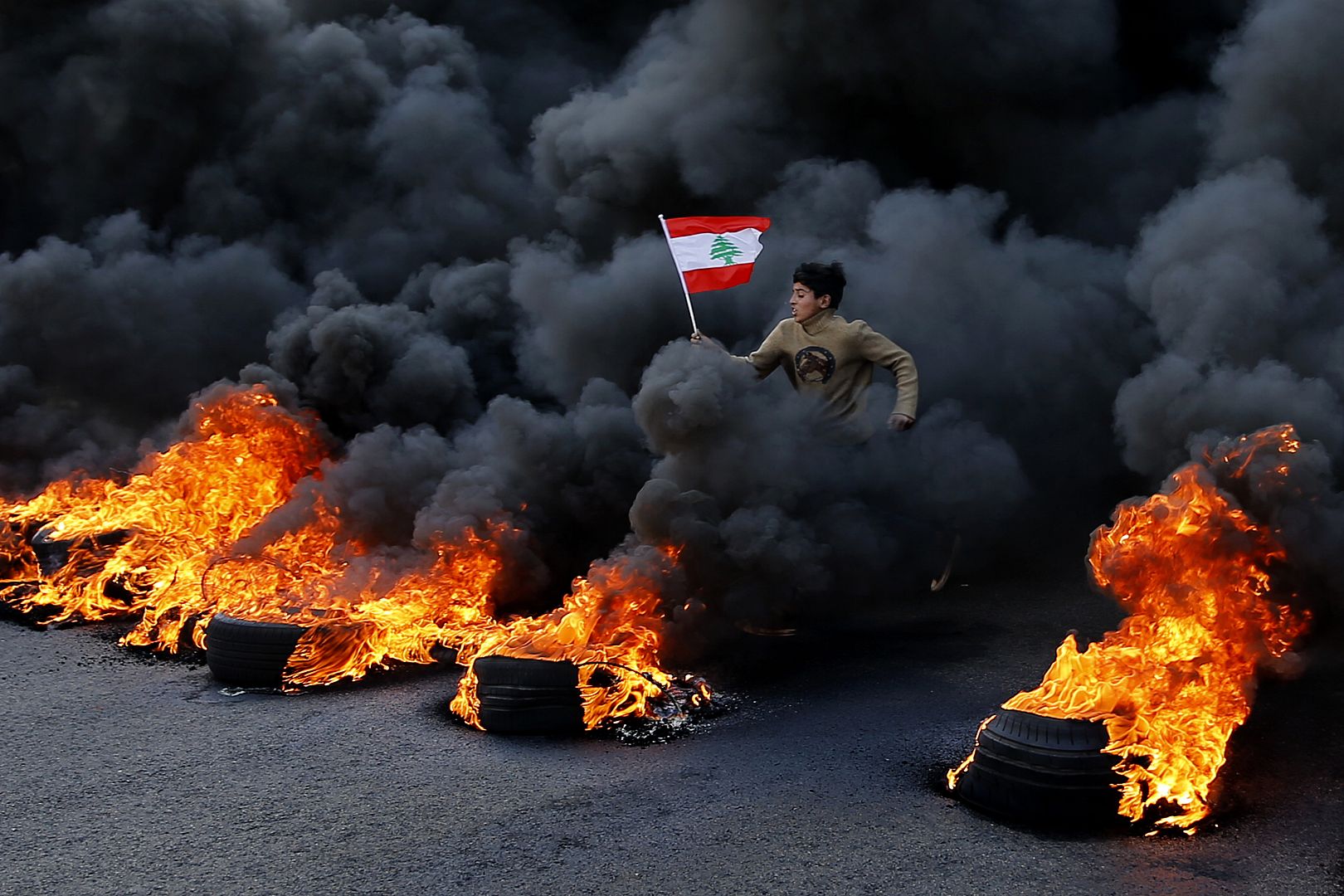 An anti-government demonstrator jumps on tires that were set on fire to block a main highway during a protest in the town of Jal el-Dib, near Beirut, Lebanon. 14 Jan. 2020.