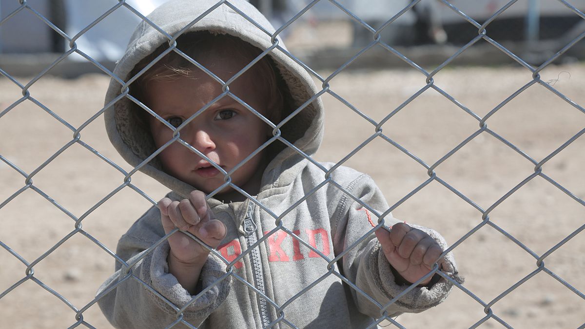 A child looks through a chain linked fence at al-Hol displacement camp