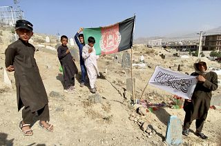 Afghan boys play with flags at a cemetery near Kabul. One group holds the former government’s flag, while the boy on the right shows what seems to be a Taliban flag.