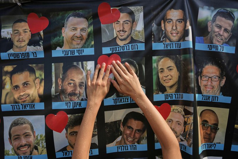 إسرائيليون يضعون ملصقًا على شكل على لافتة تحمل صور الرهائن الإسرائيليين خلال تجمع في ساحة تُعرف بـ"ساحة الرهائن" في تل أبيب بإسرائيل،13 أكتوبر 2025 