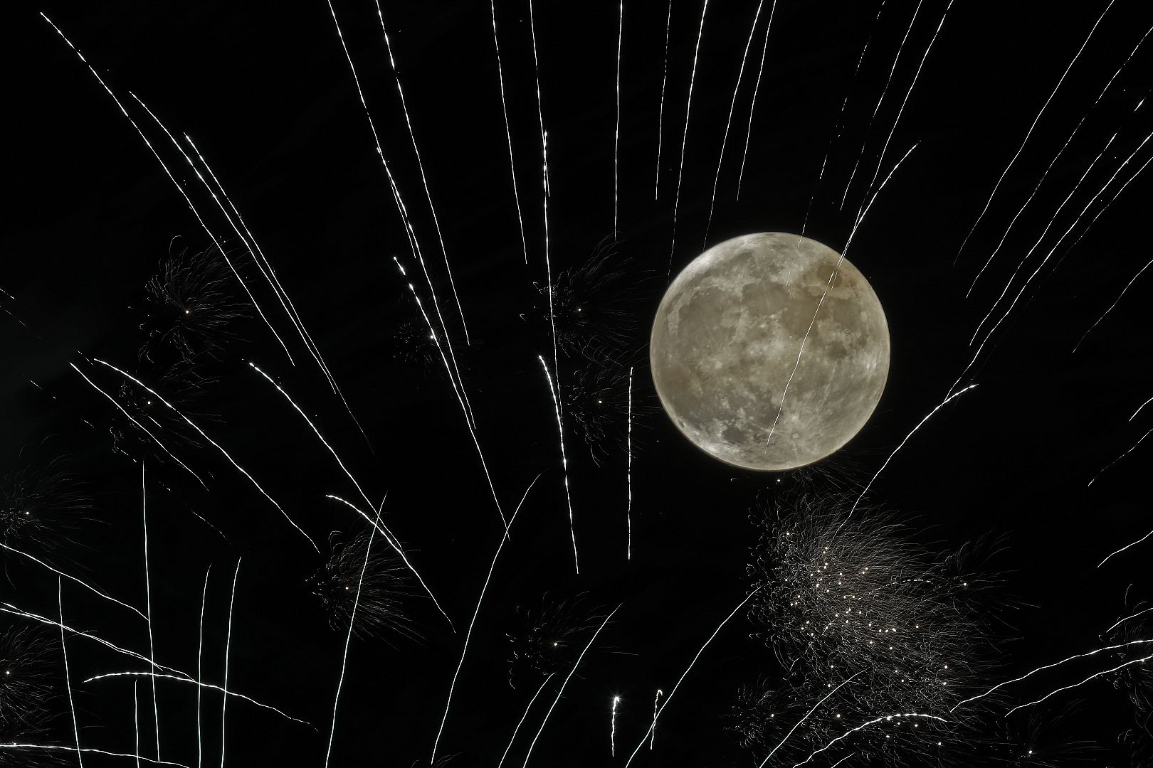 A 4th of July fireworks display lights up the sky as the full moon rises in the distance. Stillwell, Kansas, USA. 4 July 2020