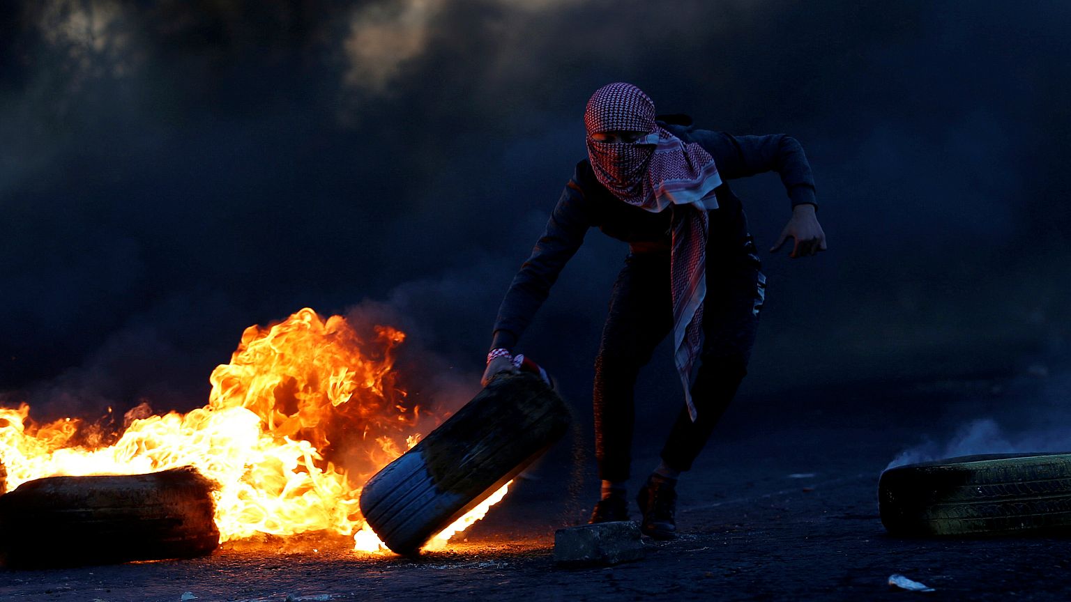 Palestinian moves a tire during clashes with Israeli troops at a protest 