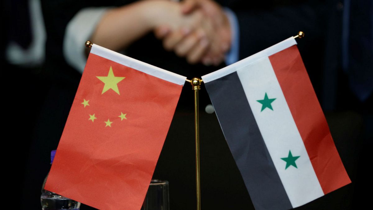 Chinese and Syrian businessmen shake hands behind their national flags 