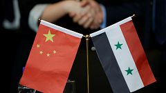 Chinese and Syrian businessmen shake hands behind their national flags 