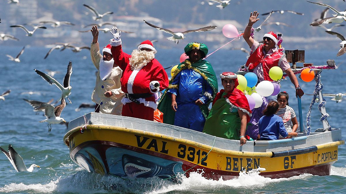 Un hombre vestido con un traje de Papa Noel saluda a la gente desde el bote