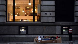 A homeless man sleeps in the cardboard box where he lives, outside Barclays