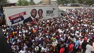 Crowds gather around a George Weah campaign poster ahead of his arrival