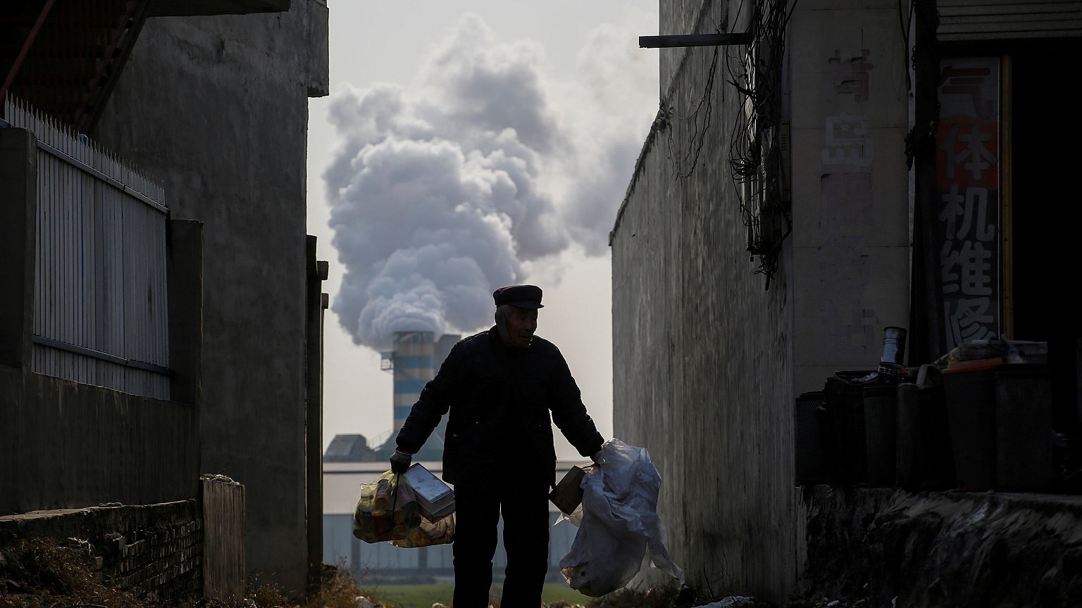 A man collects recyclables as smoke billows from a factory in Gaoyi, China