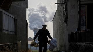 A man collects recyclables as smoke billows from a factory in Gaoyi, China