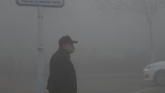 A man wearing a mask stands amid heavy fog in Jinan, Shandong province