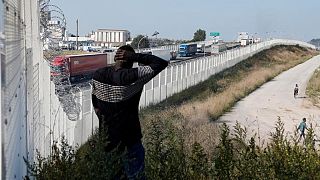 مهاجر يسير بمحاذاة سياج في كاليه يحول دون عبور المهاجرين إلى بريطانيا