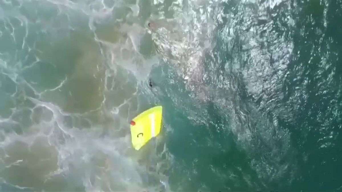 Lifeguard drone dropping float into water close to two swimmers in trouble