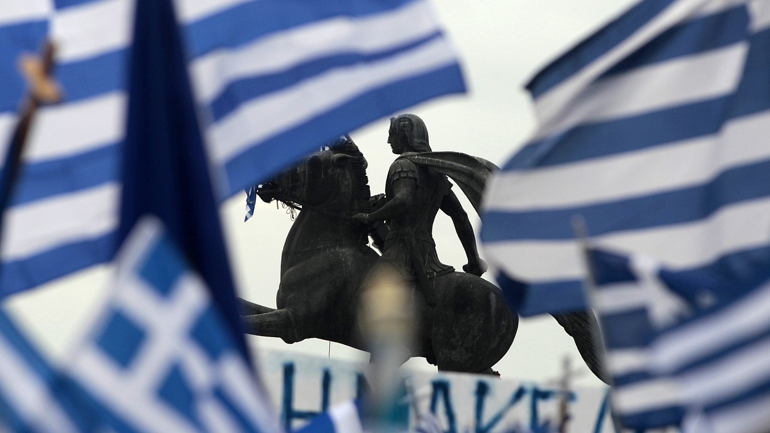 A statue of Alexander the Great is seen through waving Greek national flags