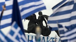 A statue of Alexander the Great is seen through waving Greek national flags