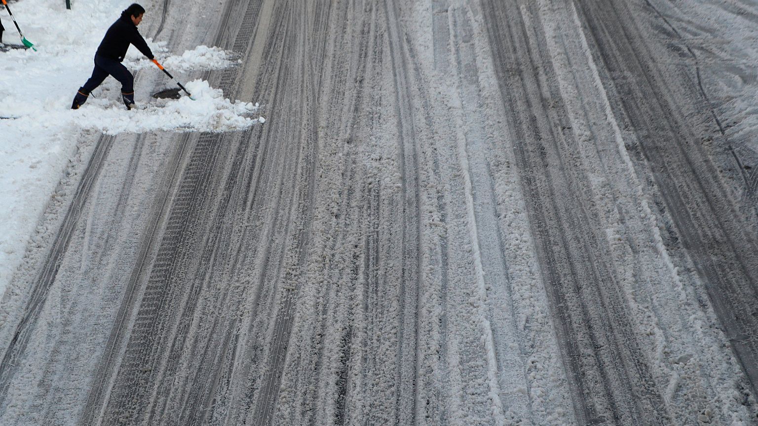 Un homme tente de balayer la neige sur une route de Tokyo.