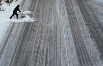 Un homme tente de balayer la neige sur une route de Tokyo.