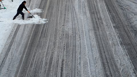 Un homme tente de balayer la neige sur une route de Tokyo.