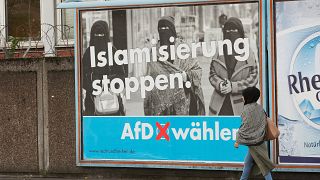 A woman with a headscarf walks past an election campaign poster of the AfD