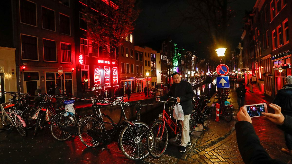 A tourist poses for a photo near a canal in the red district of Amsterdam, 