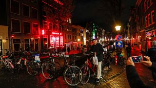 A tourist poses for a photo near a canal in the red district of Amsterdam,