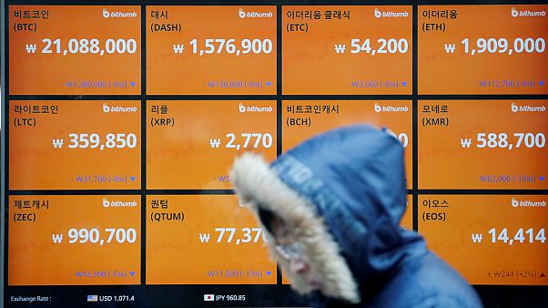 Uma pessoa passa diante de um quadro com várias taxas de "criptocâmbio" Uma pessoa passa diante de um quadro com várias taxas de "criptocâmbio"