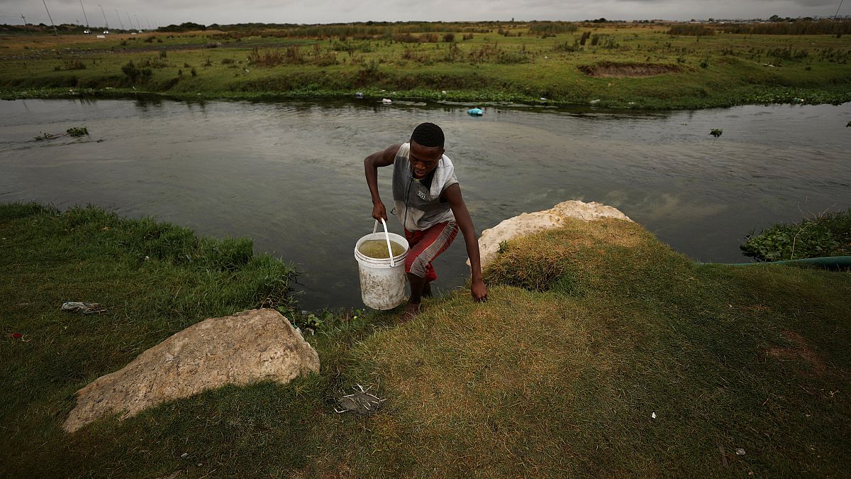 Ein Mann holt Wasser aus einem verschmutzten Fluss.